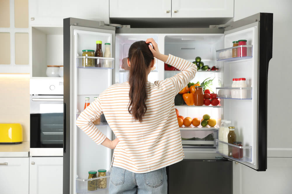 A woman scratching her head at one of the signs her fridge is dying.